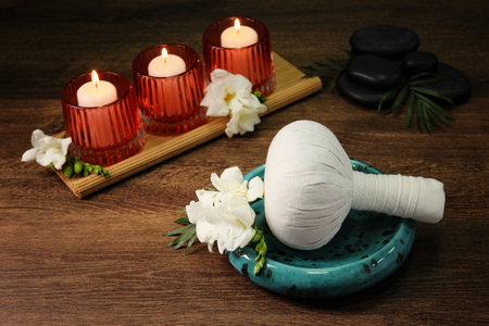 Herbal massage bag, burning candles and spa stones on wooden tableの写真素材