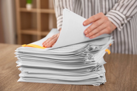 Woman stacking documents at wooden table indoors, closeup
