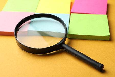 Magnifier glass and different memory stickers on orange background, closeup. Find keywords conceptの写真素材