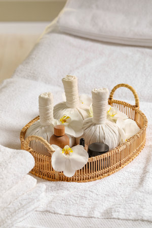 Wicker tray with herbal bags and other spa products on white bath towelの写真素材