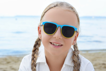 Little girl wearing sunglasses at the beach on sunny dayの写真素材