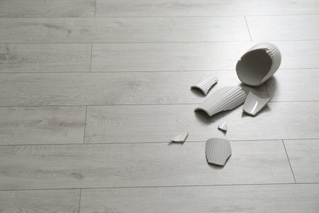 Broken ceramic vase on wooden floor. Space for text