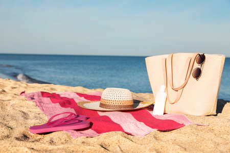 Towel with bag and beach accessories on sand near sea, space for textの写真素材