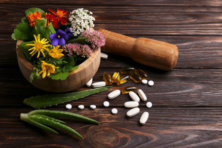 Mortar with fresh herbs, flowers and pills on wooden table, space for textの写真素材