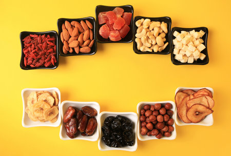 Bowls with dried fruits and nuts on yellow background, flat lay. Space for textの写真素材