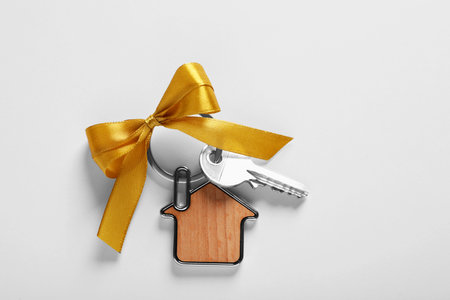 Key with trinket in shape of house and yellow bow on light gray background, top view. house warming partyの写真素材