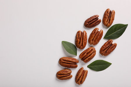 Delicious pecan nuts and green leaves on white background, flat lay. Space for textの写真素材