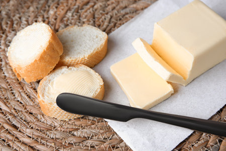 Tasty cut baguette with fresh butter on wicker mat, closeup