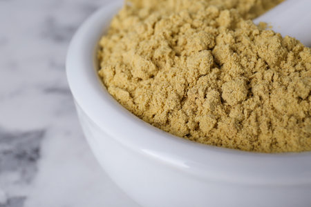 Mortar with aromatic mustard powder on white marble table, closeup