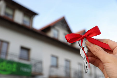 Woman holding key with bow near house outdoors, closeup. Space for textの写真素材