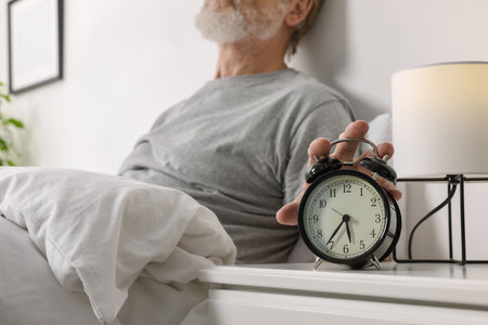 Man turning off alarm clock in bedroom, closeupの写真素材