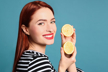 Happy woman with red dyed hair and lemons on light blue backgroundの写真素材