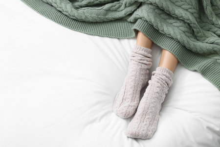 Woman wearing warm socks in comfortable bed, above view. Space for textの写真素材