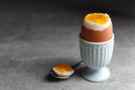 Fresh soft boiled egg in cup on gray table, closeup. Space for textの写真素材