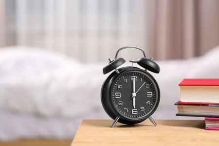 Black alarm clock and books on wooden table indoors. Space for textの写真素材