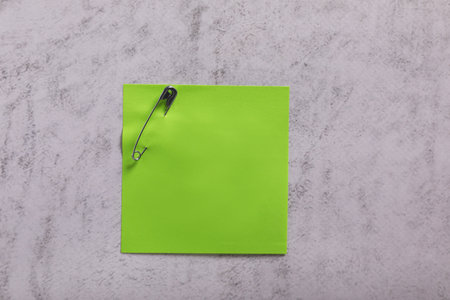 Green paper note with safety pin on gray textured background, top viewの写真素材