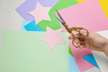 Woman holding beautiful scissors near colorful paper sheets on white wooden table, closeup. Space for textの写真素材