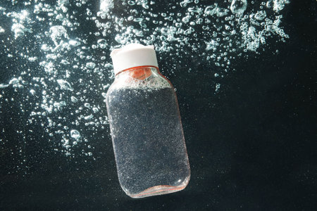 Bottle of micellar water in liquid with bubbles on black background