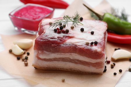 Piece of tasty pork fatback with peppercorns and garlic on white table, closeupの写真素材