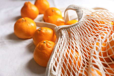 Net bag with many fresh ripe tangerines on white cloth, closeupの写真素材
