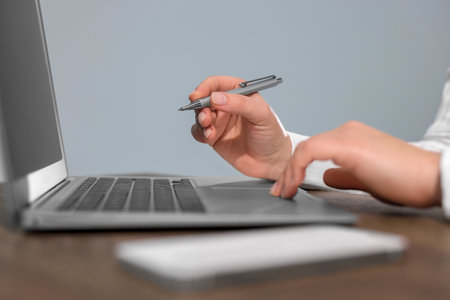 Woman with smartphone and pen working on laptop at wooden table, closeup. Electronic document managementの写真素材