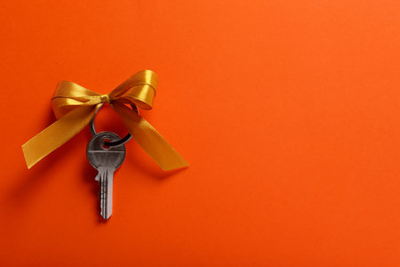 Key with yellow bow on orange background, top view. Space for text. house warming party
