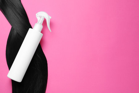 Spray bottle with thermal protection and lock of brunette hair on pink background, flat lay. Space for textの写真素材