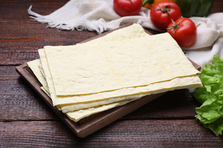 Delicious folded Armenian lavash and fresh vegetables on wooden table, closeup
