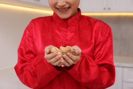 Young woman holding bowl of tasty fortune cookies with predictions in kitchen, closeupの写真素材