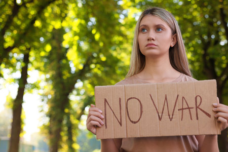 Sad woman holding poster with words No War in park. Space for textの写真素材