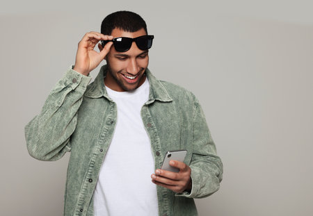 Smiling African American man in sunglasses with smartphone on light gray background. Space for text