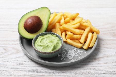 Plate with french fries, guacamole dip and avocado served on white wooden tableの写真素材