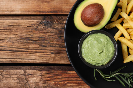 Plate with french fries, guacamole dip and avocado served on wooden table, top view. Space for textの写真素材