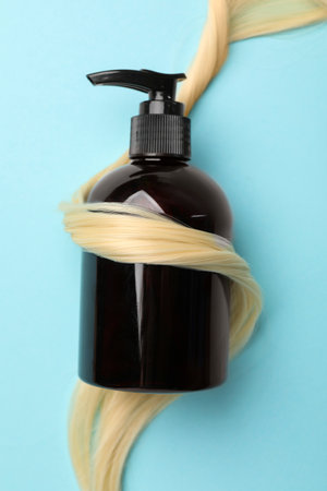 Shampoo bottle wrapped in lock of hair on light blue background, top viewの写真素材