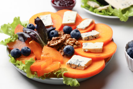 Delicious persimmon with blue cheese, blueberries, lettuce and walnuts on white table, closeupの写真素材