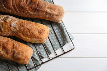 Fresh crispy ciabattas on white wooden table, top view. Space for text