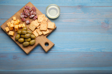 Toothpick appetizers. Pieces of cheese, sausage, olives and crackers on light blue wooden table, flat lay. Space for textの写真素材