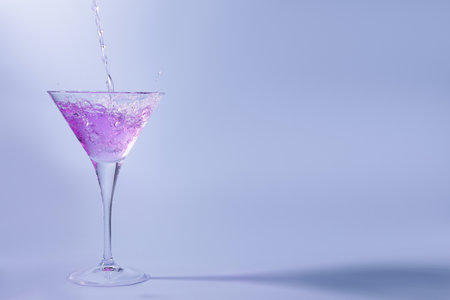 Pouring fresh cocktail into martini glass on light blue background, space for textの写真素材