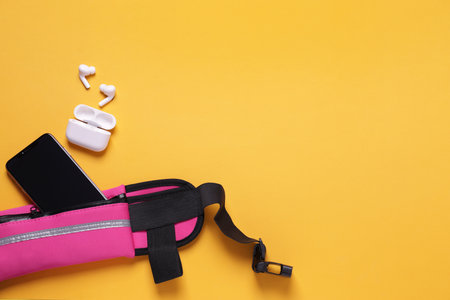 Stylish pink waist bag with smartphone and earphones on orange background, flat lay. Space for textの写真素材