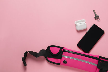 Stylish waist bag with smartphone, key and earphones on pink background, flat lay. Space for textの写真素材