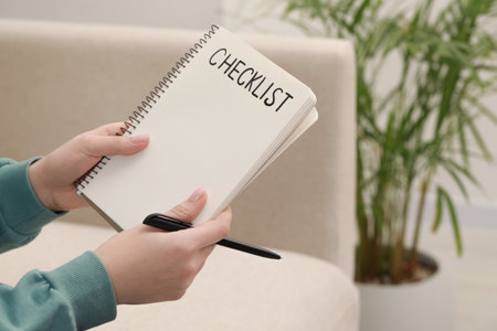 Woman holding notebook with inscription Checklist and pen indoors, closeup. Space for textの写真素材