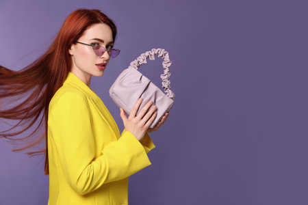 Stylish woman with red dyed hair and bag on purple background, space for textの写真素材