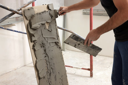 Worker spreading adhesive mix over tile with spatula, closeupの写真素材
