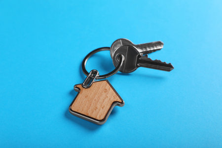 Keys with trinket in shape of house on blue background, closeup. real estate agent services