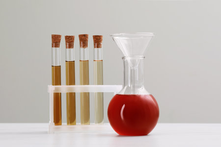 Different laboratory glassware with brown liquids on white table against light background