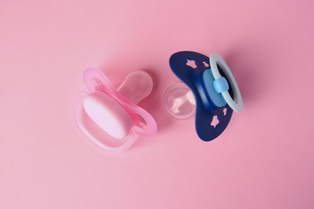 Colorful baby pacifiers on pink background, flat lay