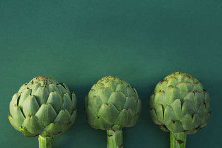 Whole fresh raw artichokes on green background, flat lay. Space for textの写真素材