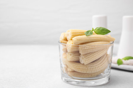 Canned baby corns with basil on white table, closeup. Space for textの写真素材