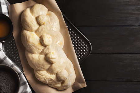 Raw braided bread and ingredients on black wooden table, flat lay with space for text. Traditional...