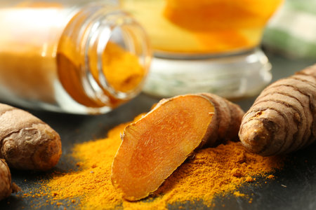 Turmeric roots, powder and cup of tasty tea on black table, closeupの写真素材